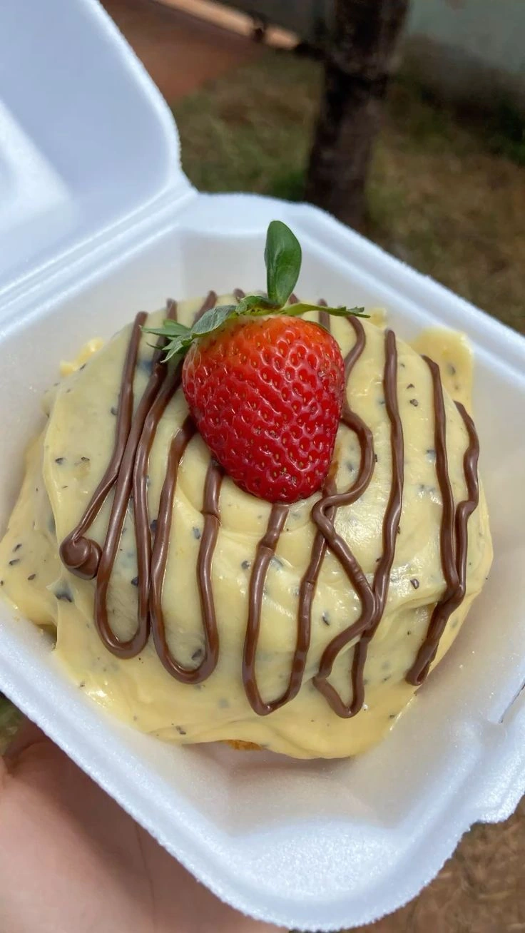 Mini bolo com cobertura cremosa clara, fios de chocolate e um morango na decoração