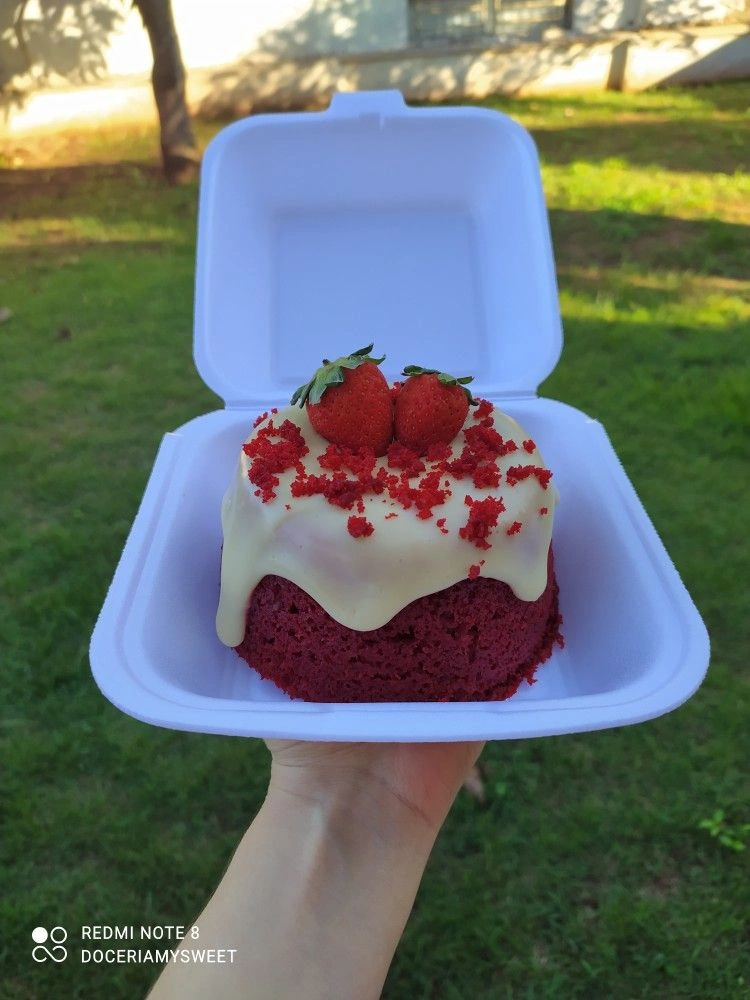 Mini bolo de massa vermelha com cobertura clara, farelos vermelhos e morangos